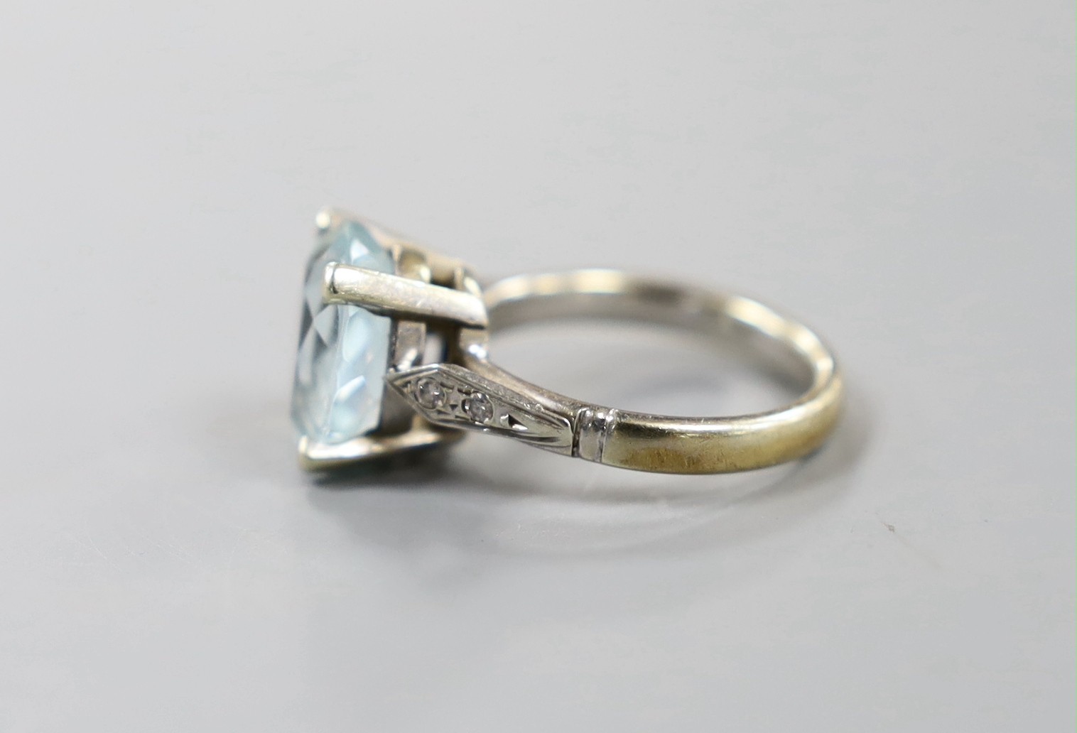 A modern yellow and white metal, oval cut aquamarine set dress ring, with diamond chip set shoulders, size N, gross weight 5.6 grams.